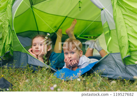 Children are enjoying a peaceful time inside a cozy green tent on a lovely day, amid the stunning beauty of nature Children are enjoying a peaceful time inside a cozy green tent on a lovely day, amid the stunning beauty of nature 119527682