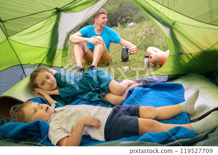 In a family camping scene, the children relax in their tent while dad cooks delicious meals outside 119527709