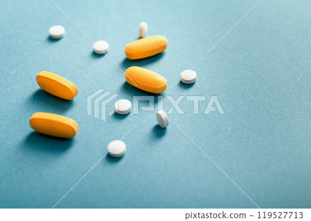 Closeup of white and yellow medical pills or Dietary supplement on a blue background with space for text. Closeup of white and yellow medical pills or Dietary supplement on a blue background with space for text. 119527713