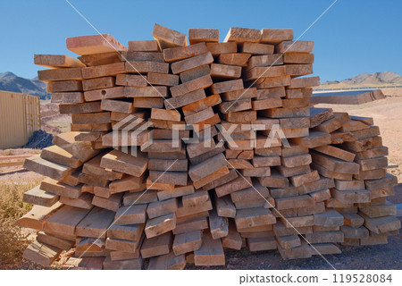 Stack of wooden planks with arid landscape behind. Construction materials in desert Stack of wooden planks with arid landscape behind. Construction materials in desert 119528084