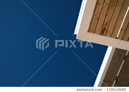 Minimalist architectural corner. White and wood roof structure against blue sky Minimalist architectural corner. White and wood roof structure against blue sky 119528089