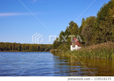 A tranquil lake scene with a cozy house hidden by trees A tranquil lake scene with a cozy house hidden by trees 119528135