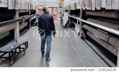 Customer leisurely browses flooring options in a hardware store, carefully selecting materials for an exciting renovation project. A man in a hardware store choosing flooring. 119528226
