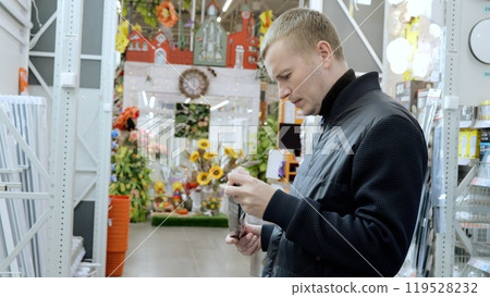 Man carefully examines the product packaging while shopping in a hardware store to make an informed choice. A man in a hardware store, choosing materials for repairs. 119528232