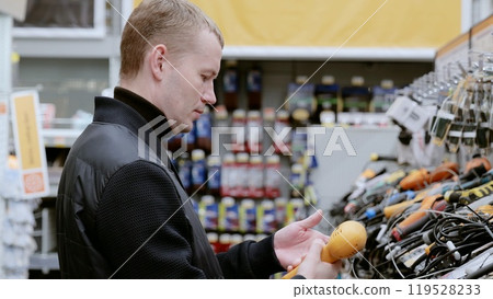 Man browsing heat guns in a hardware store, surrounded by construction tools, in a lively consumer environment. A man in a hardware store choosing a tool. Man browsing heat guns in a hardware store, surrounded by construction tools, in a lively consumer environment. A man in a hardware store choosing a tool. 119528233