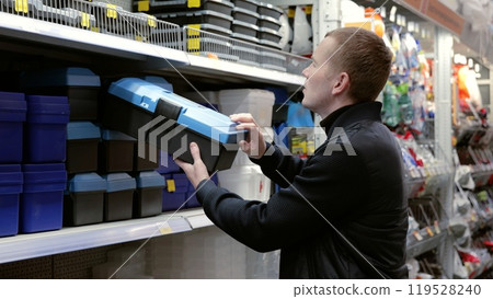 Handyman carefully selecting a toolbox in a hardware store before making a purchase. A man in a hardware store choosing a tool. 119528240