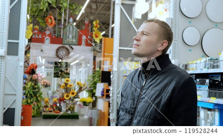 Man carefully considers lighting options for his apartment renovation while browsing through a wide selection of fixtures in a home improvement store 119528244