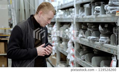 Man is carefully selecting plumbing supplies in a hardware store, using his smartphone to compare products and make informed decisions 119528260