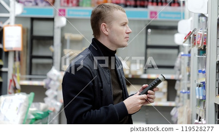 A man chooses hygiene products in a supermarket, shelves with shampoos. Shopper carefully selects a hair conditioner from the supermarket shelf and reads the label on the bottle A man chooses hygiene products in a supermarket, shelves with shampoos. Shopper carefully selects a hair conditioner from the supermarket shelf and reads the label on the bottle 119528277
