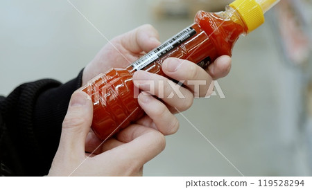 A customer in black studies the label on a bottle of sauce. Shopper diligently scrutinizes the nutrition facts on a hot sauce label at the supermarket, opting for a healthier option A customer in black studies the label on a bottle of sauce. Shopper diligently scrutinizes the nutrition facts on a hot sauce label at the supermarket, opting for a healthier option 119528294