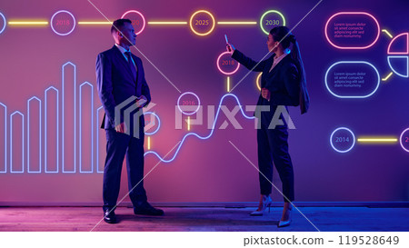 Two speakers stands in front of vibrant graphs, pointing out key data insights in professional meeting. Two speakers stands in front of vibrant graphs, pointing out key data insights in professional meeting. 119528649