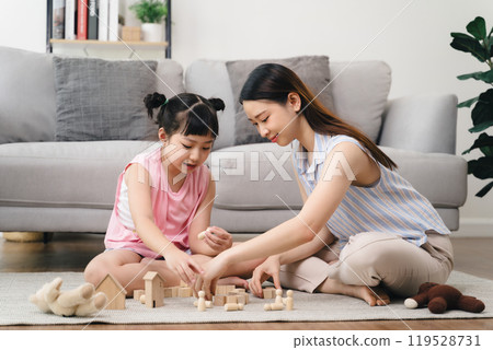A woman and a little girl are playing with wooden blocks on a carpeted floor 119528731