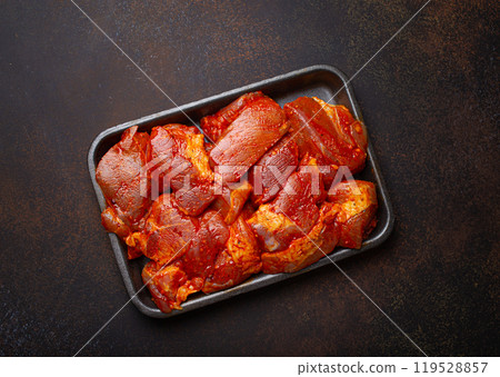 Raw uncooked chopped pieces of pork marinade with seasonings in black plastic container top view on dark rustic background. Preparing meal with marinated pork fillet pieces Raw uncooked chopped pieces of pork marinade with seasonings in black plastic container top view on dark rustic background. Preparing meal with marinated pork fillet pieces 119528857