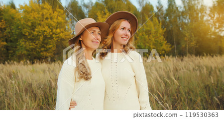 Happy two women friends looking away in autumn park, stylish smiling girlfriends standing outdoors Happy two women friends looking away in autumn park, stylish smiling girlfriends standing outdoors 119530363