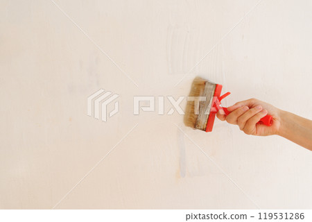 Person is holding brush with glue on background of light wall. apply thick wallpaper glue.  119531286