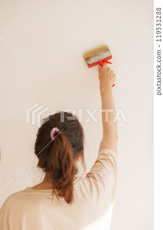 Woman holds brush with glue against light wall apply thick wallpaper glue. Ready to paste wallpaper 119531288