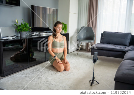 Young woman doing sport exercise using a sports app on her mobile phone at home. Online training concept 119532054