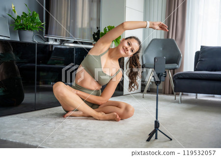 Young woman doing sport exercise using a sports app on her mobile phone at home. Online training concept Young woman doing sport exercise using a sports app on her mobile phone at home. Online training concept 119532057