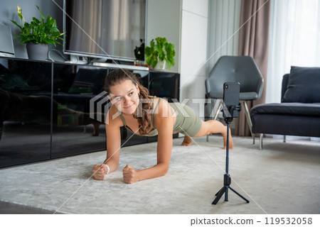 Young woman doing sport exercise using a sports app on her mobile phone at home. Online training concept Young woman doing sport exercise using a sports app on her mobile phone at home. Online training concept 119532058