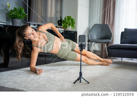 Young woman doing sport exercise using a sports app on her mobile phone at home. Online training concept Young woman doing sport exercise using a sports app on her mobile phone at home. Online training concept 119532059