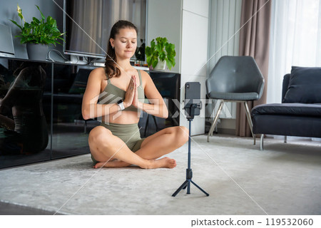 Young woman doing yoga using a sports app on her mobile phone at home. Online training concept Young woman doing yoga using a sports app on her mobile phone at home. Online training concept 119532060