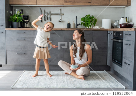 Mother and daughter sitting on kitchen floor, eating or having a breakfast and playing. Family bonding Mother and daughter sitting on kitchen floor, eating or having a breakfast and playing. Family bonding 119532064