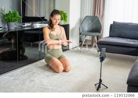 Young woman looking at fitness tracker on smart watch during doing sport exercise using a sports app on her mobile phone at home. Online training concept. Young woman looking at fitness tracker on smart watch during doing sport exercise using a sports app on her mobile phone at home. Online training concept. 119532066