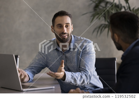 Positive handsome Latin businessman talking to business partner at workplace 119532502