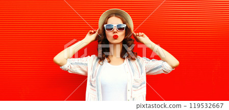 Portrait of beautiful young woman blowing kiss posing wearing a summer straw hat on red background Portrait of beautiful young woman blowing kiss posing wearing a summer straw hat on red background 119532667