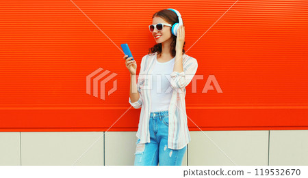 Portrait of smiling young woman in headphones listening to music with smartphone on red background 119532670