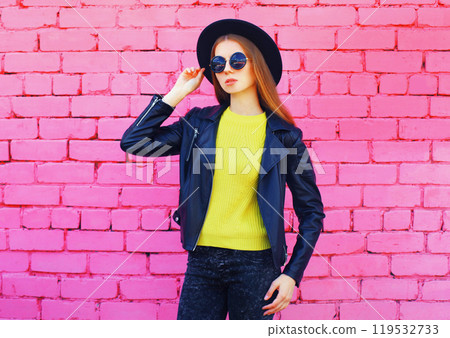 Fashion young woman wearing a black hat, jacket on colorful pink bricks background 119532733