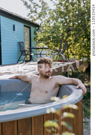 Man relaxing solo in a hot tub, enjoying peace and nature in a serene outdoor setting Man relaxing solo in a hot tub, enjoying peace and nature in a serene outdoor setting 119533454