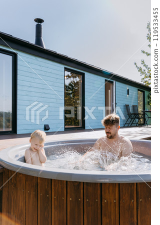 Father and son bonding in backyard hot tub, splashing water, enjoying outdoor family time under sun Father and son bonding in backyard hot tub, splashing water, enjoying outdoor family time under sun 119533455