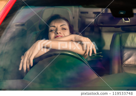 A woman is laying in a car with her hands on her face. She is smiling and she is relaxed. 119533748
