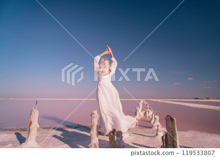 Woman White Dress Pink Salt Lake Landscape Photography. She stands on a pink salt flat with a blue sky in the background. 119533807