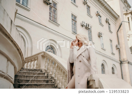 A woman in a white coat stands on a white staircase in front of a building. She is smiling and she is enjoying herself. A woman in a white coat stands on a white staircase in front of a building. She is smiling and she is enjoying herself. 119533823