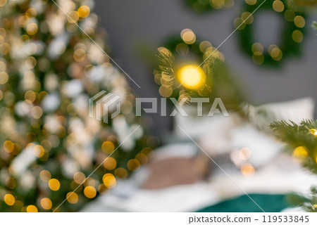 A Christmas tree is surrounded by a wreath and a bed with pillows. The room is decorated with Christmas lights and the bed is covered with a green blanket. A Christmas tree is surrounded by a wreath and a bed with pillows. The room is decorated with Christmas lights and the bed is covered with a green blanket. 119533845