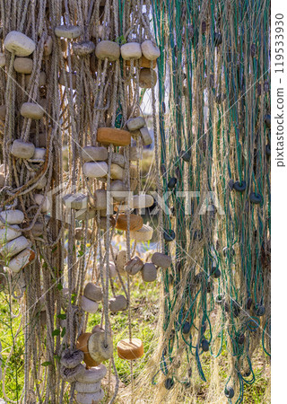 Colorful fishing floats dangle hang alongside frayed nets in a coastal area Colorful fishing floats dangle hang alongside frayed nets in a coastal area 119533930