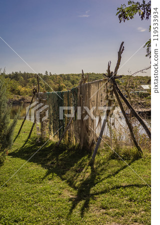 Old Fishing nets drying in the sunlight, stretched between wooden poles near a calm water 119533934