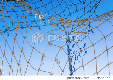 Close up of old fishing net against a clear blue sky Close up of old fishing net against a clear blue sky 119533936