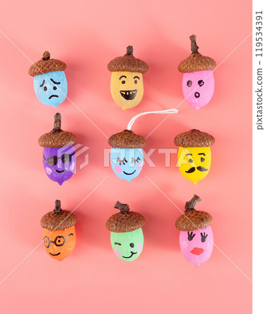 The acorns are arranged in a 3x3 grid on a light pink background. Each acorn has a brown cap and a painted face that depicts a unique expression, 119534391