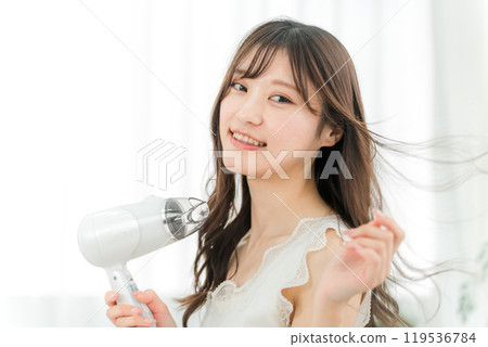 A woman blow-drying her hair with a hair dryer (hair care) 119536784