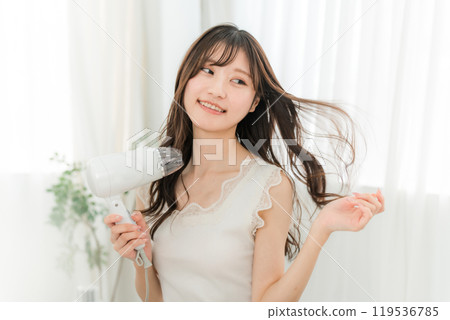 A woman blow-drying her hair with a hair dryer (hair care) 119536785