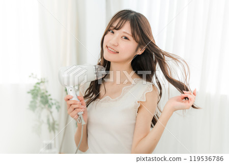 A woman blow-drying her hair with a hair dryer (hair care) 119536786