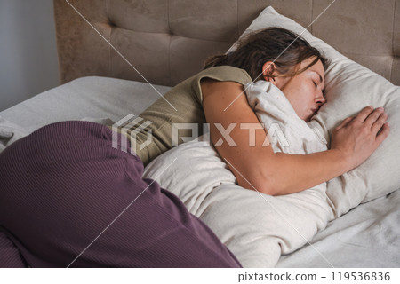 Woman peacefully sleeping with pillow in cozy bedroom setting. 119536836