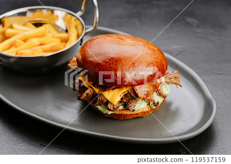 Juicy bacon cheeseburger with fries served on a stylish plate, perfect for a satisfying meal 119537159