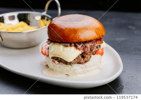 Gourmet burger with cheese, chimichurri, and fries, served on a stylish plate for an indulgent treat Gourmet burger with cheese, chimichurri, and fries, served on a stylish plate for an indulgent treat 119537174
