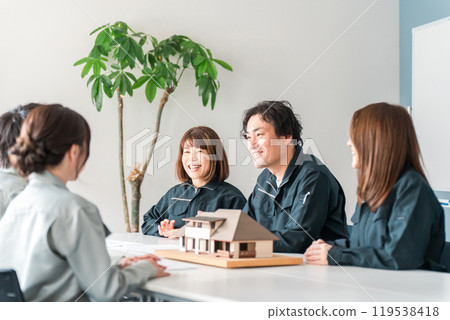 穿著工作服的建築業男性和女性商人使用房屋模型進行商務談判、解釋和演示 穿著工作服的建築業男性和女性商人使用房屋模型進行商務談判、解釋和演示 119538418