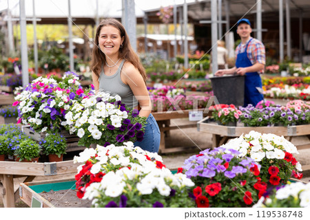 In flower shop, girl chooses ampel petunias Surfinia plant to decorate room, balcony, terrace 119538748