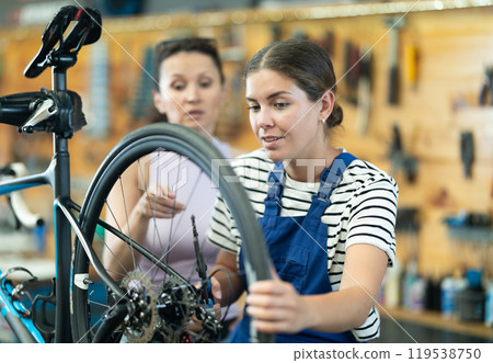 Female bicycle technician explaining repair details to client in workshop Female bicycle technician explaining repair details to client in workshop 119538750